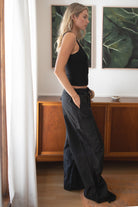 Woman wearing a black tank top and TIC TOC PH29131 TOMY black crinkled nylon parachute cargo pants with adjustable drawstring waistband and wide-leg silhouette indoors