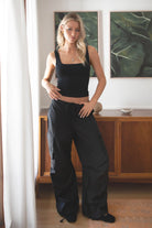 Woman wearing a black tank top and TIC TOC PH29131 TOMY black crinkled nylon parachute cargo pants with adjustable drawstring waistband and wide-leg silhouette indoors