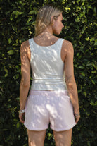 Woman wearing the TIC TOC PJ31004 CARLY pale pink cloud fleece low rise shorts featuring an elastic waistband with drawcord, deep side pockets, and raw cut hemline paired with a white tank top