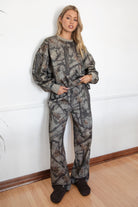 Person wearing a camouflage outfit standing against a white wall.