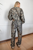 Person wearing a camouflage outfit standing against a white wall.