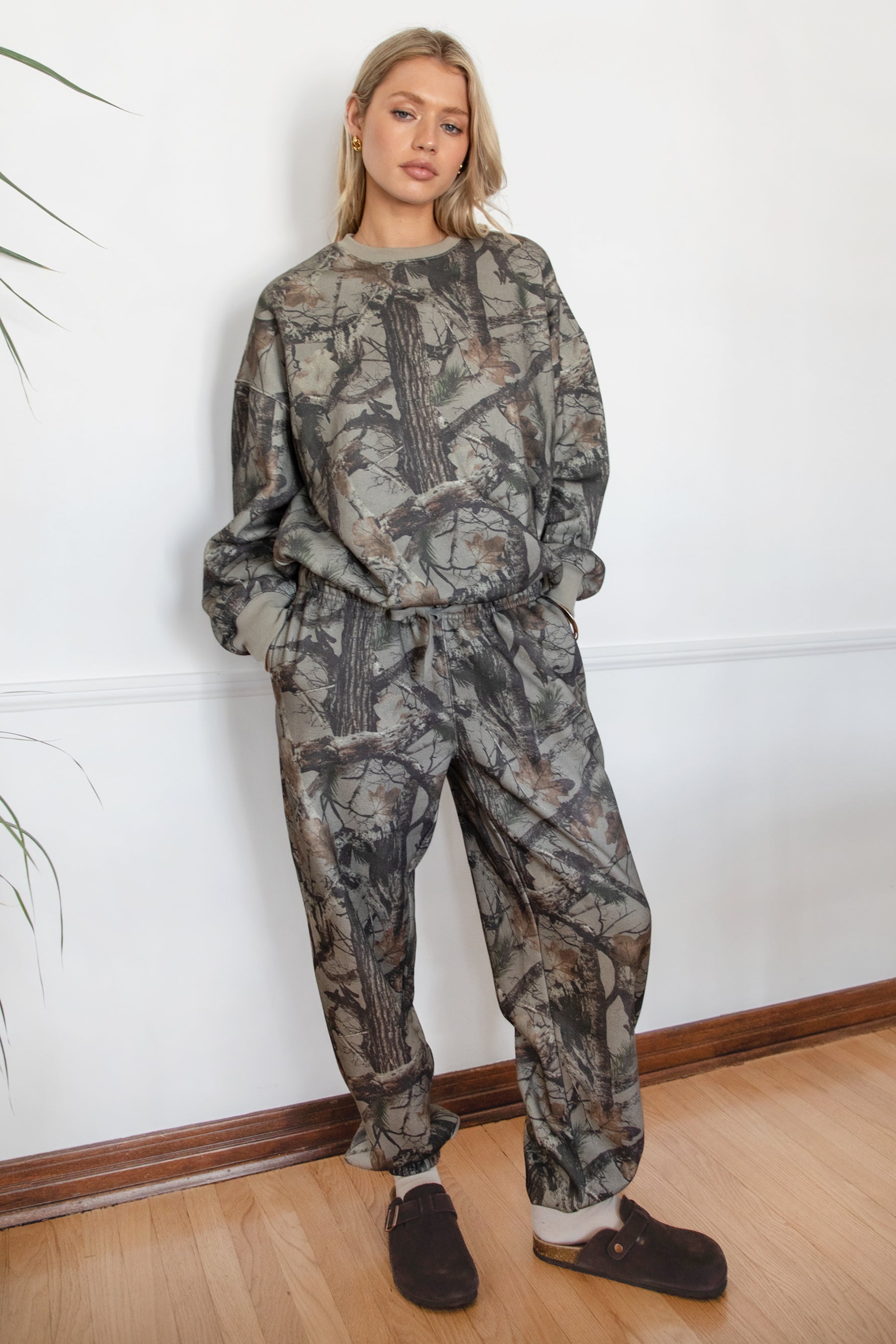 Person wearing a camouflage outfit standing against a white wall.