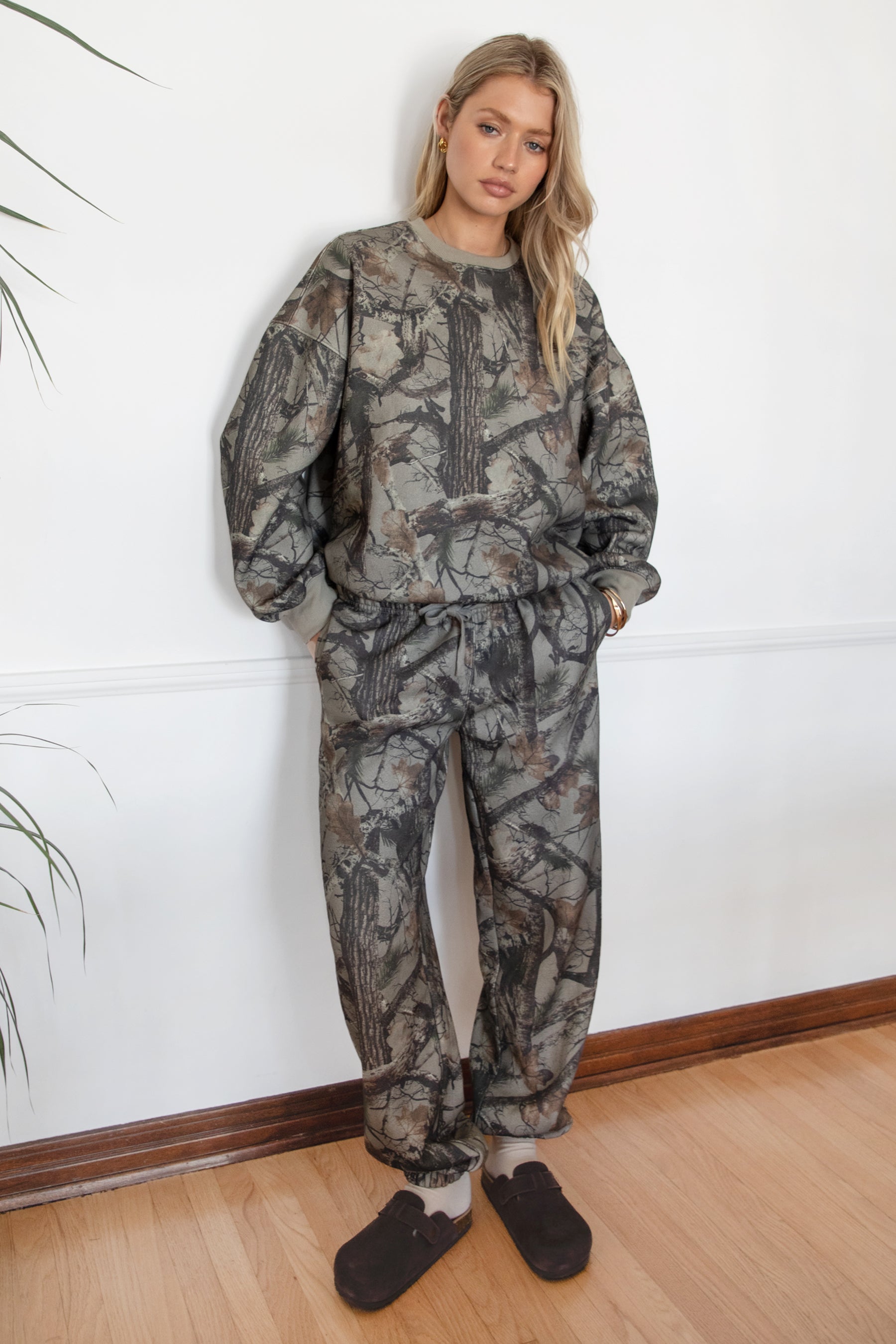 Person wearing a camouflage outfit standing against a white wall.