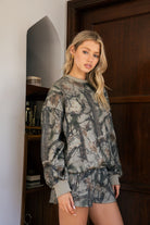 Woman wearing a camouflage outfit standing in a room with wooden door and shelves.