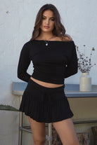 Woman wearing the TIC TOC SC31643BA CHIA black mini skirt with built-in shorts featuring drop waist design, frill hem detail, and drawstring waistband paired with the matching top outdoors. 