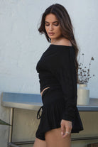 Woman wearing the TIC TOC SC31643BA CHIA black mini skirt with built-in shorts featuring drop waist design, frill hem detail, and drawstring waistband paired with the matching top outdoors. 