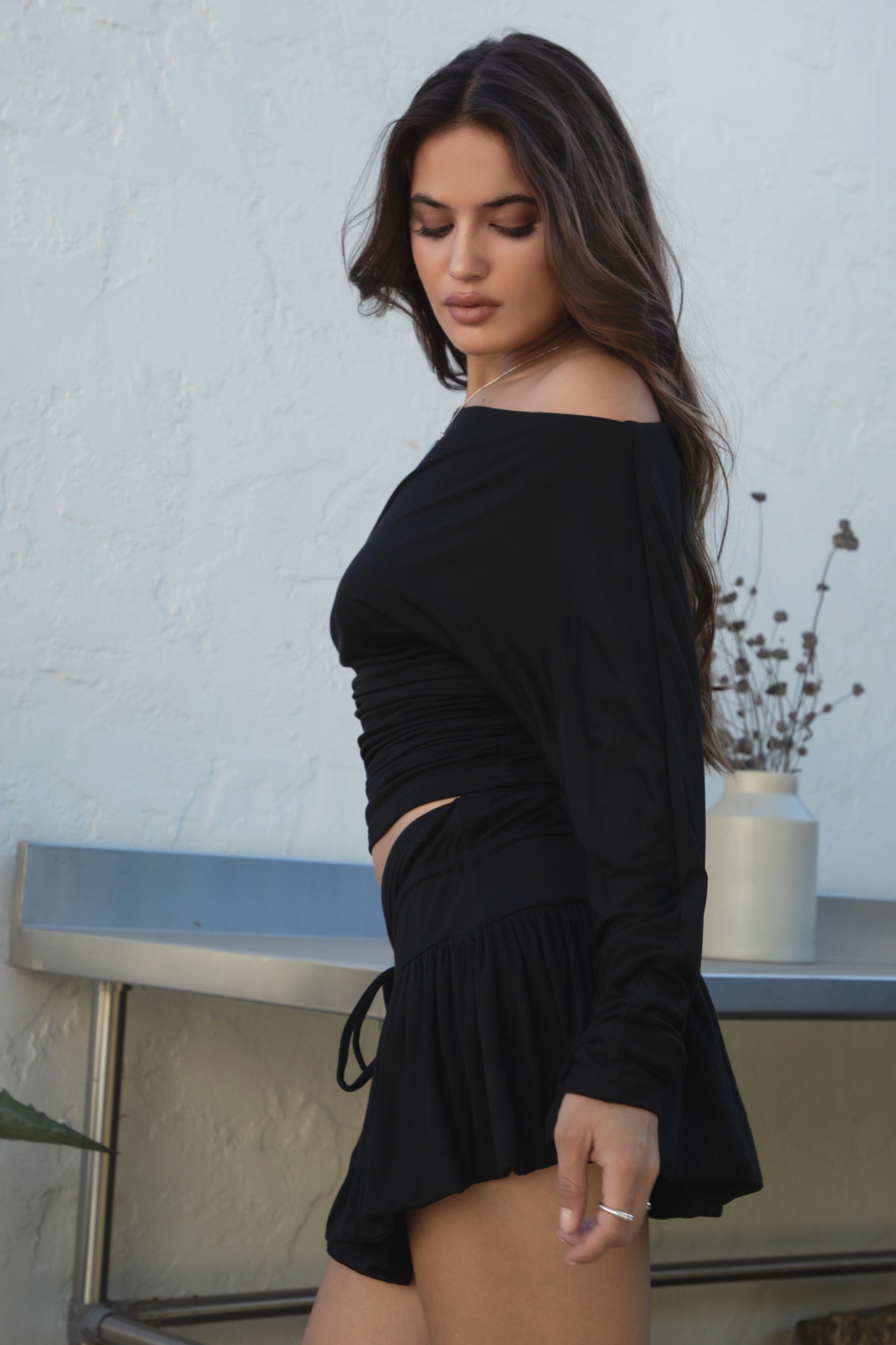 Woman wearing the TIC TOC SC31643BA CHIA black mini skirt with built-in shorts featuring drop waist design, frill hem detail, and drawstring waistband paired with the matching top outdoors. 