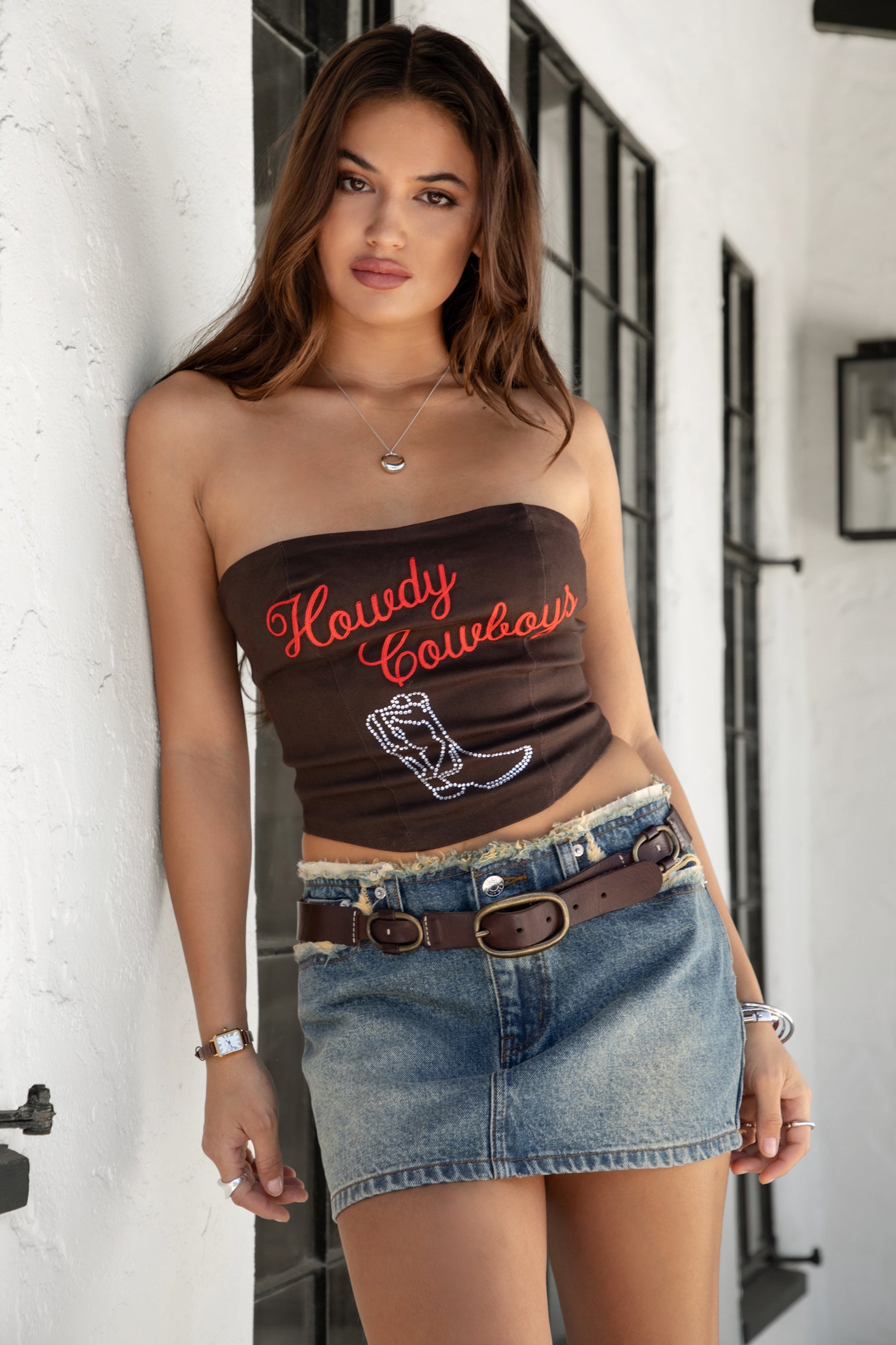 Woman wearing TIC TOC SF31900 JASMI washed denim low rise mini skirt with raw hem, vintage wash, and Y2K silhouette paired with a strapless western top.