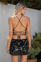 Model wearing the TIC TOC SL31480 VEDA black chiffon beaded low-rise mini skort featuring hand-beaded floral embroidery, chiffon overlay, and built-in shorts with a matching cami top in an outdoor setting. 