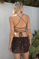 Model wearing the TIC TOC SL31480 VEDA brown chiffon beaded low-rise mini skort featuring hand-beaded floral embroidery, chiffon overlay, and built-in shorts with matching cami top in an outdoor setting. 