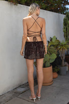 Model wearing the TIC TOC SL31480 VEDA brown chiffon beaded low-rise mini skort featuring hand-beaded floral embroidery, chiffon overlay, and built-in shorts with matching cami top in an outdoor setting. 