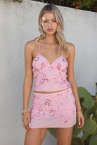 Model wearing the TIC TOC SL31480 VEDA pink chiffon beaded low-rise mini skort featuring hand-beaded floral embroidery, chiffon overlay, and built-in shorts with a matching cami top in an outdoor setting. 