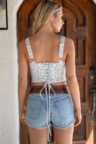 Woman wearing a floral crop top and denim shorts standing in front of a wooden door.