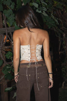 Woman wearing the TIC TOC TA31523 SADELIA khaki stretch suede embroidered strapless top featuring western embroidery, lace-up back, and curved hem paired with brown denim pants. 