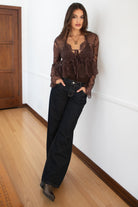 Model wearing the TIC TOC TA31608 LAREDA brown crochet embroidered long sleeve top featuring a scalloped V-neckline, tie front detail, and flowy bell sleeves with dark denim jeans. 