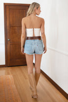 Woman wearing TIC TOC TA31611 RALLYE white stretch twill strapless top with sequin GAME DAY patch and lace-up back paired with a white skirt with brown boots in a room.