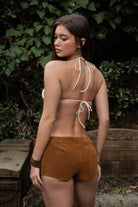 Woman wearing TIC TOC PH31284 MOOEDY-BT faux cow fur bra top featuring ultra-soft cow print fur cups, adjustable halter tie straps, slim back tie closure, and minimal triangle silhouette styled with brown festival shorts in an outdoor western-inspired setting.