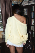 Person wearing a yellow sweater and white skirt in a room with bookshelves.