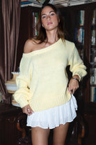 Woman wearing a yellow off-shoulder sweater and white skirt in a room with bookshelves.