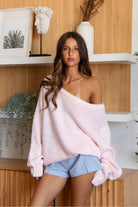 Woman wearing a pink sweater and checkered shorts in a room with wooden walls and shelves.
