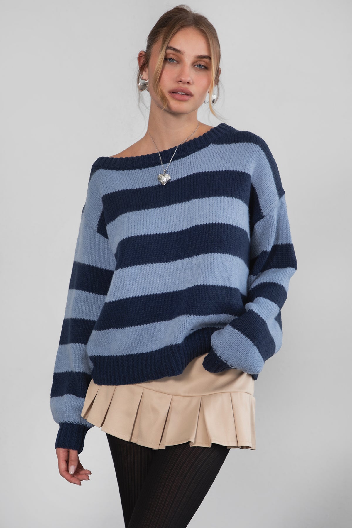 A woman wearing a TIC TOC TC30623 Maddee navy blue rugby knit oversized sweater with an off-the-shoulder neckline and striped color block design, paired with a beige skirt