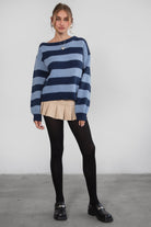 A woman wearing a TIC TOC TC30623 Maddee navy blue rugby knit oversized sweater with an off-the-shoulder neckline and striped color block design, paired with a beige skirt