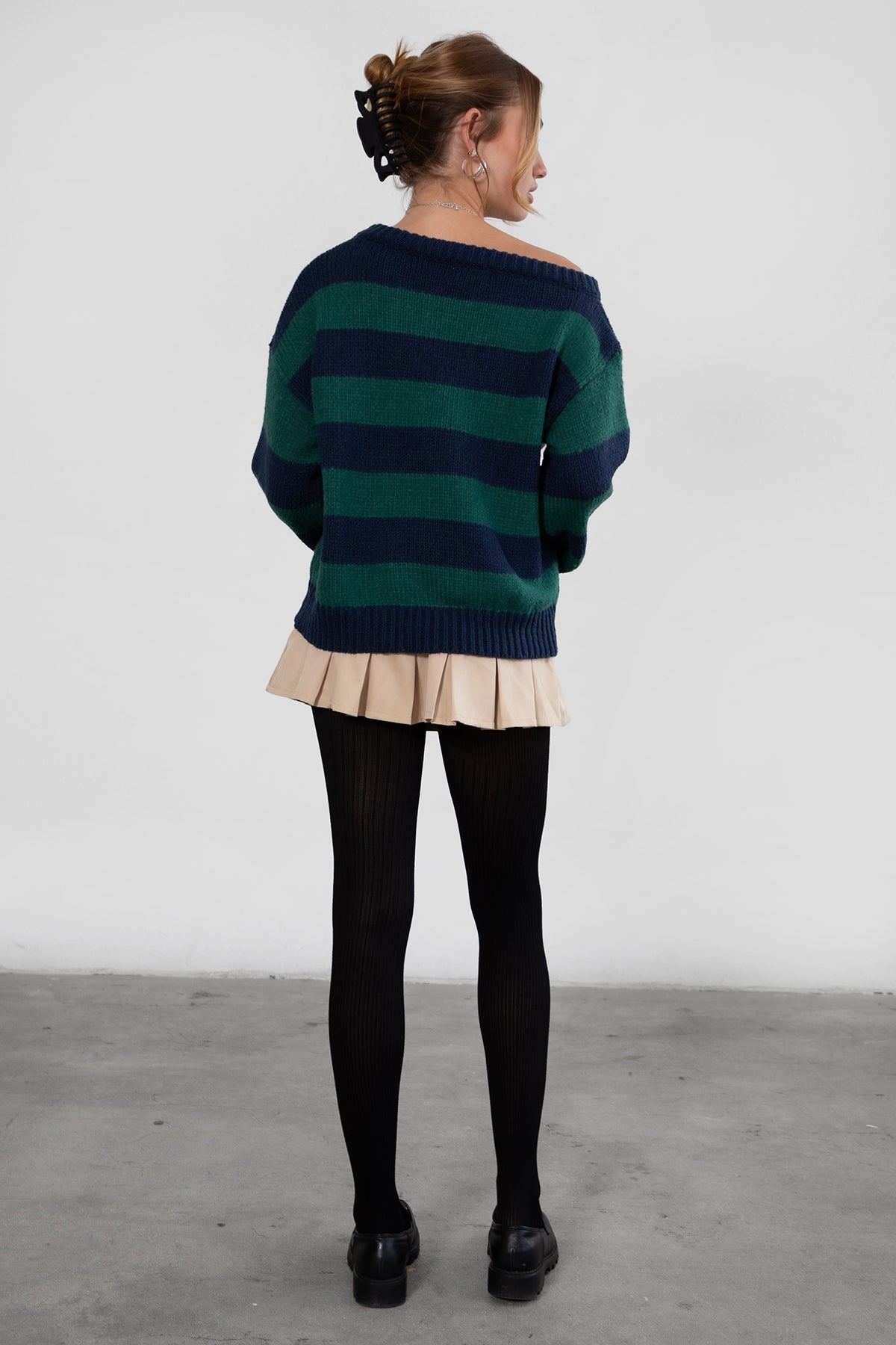 A woman wearing a TIC TOC TC30623 Maddee navy green rugby knit oversized sweater with an off-the-shoulder neckline and striped color block design, paired with a beige skirt