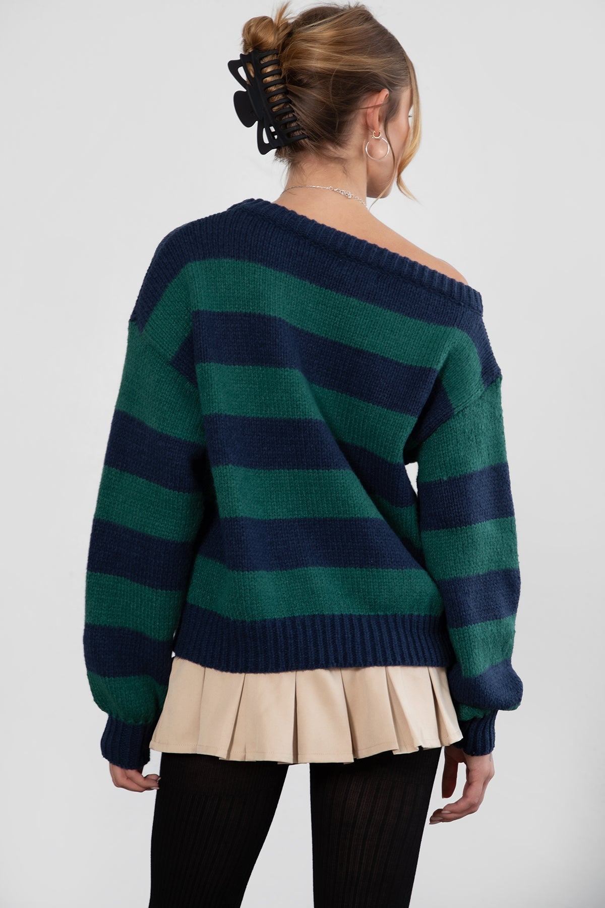 A woman wearing a TIC TOC TC30623 Maddee navy green rugby knit oversized sweater with an off-the-shoulder neckline and striped color block design, paired with a beige skirt