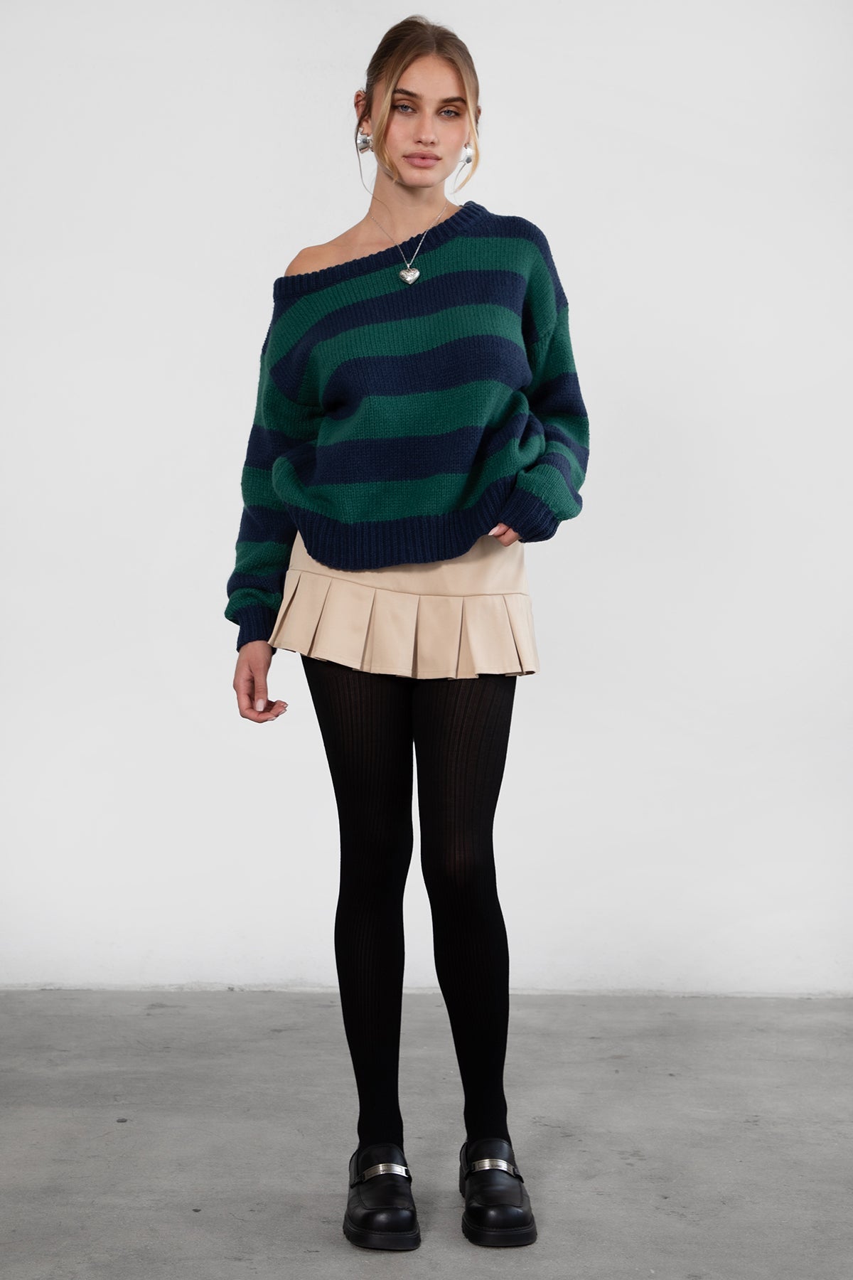A woman wearing a TIC TOC TC30623 Maddee navy green rugby knit oversized sweater with an off-the-shoulder neckline and striped color block design, paired with a beige skirt