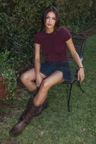 Model wearing the TIC TOC TC31437 LAURENI black cherry cable knit short sleeve top featuring a cropped silhouette, crew neckline, and textured knit design paired with a denim pleated mini skirt outdoors
