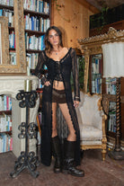 Woman in a black lace outfit standing in a room with bookshelves and decorative elements.