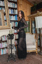 Woman in a black dress standing in a room with bookshelves and decorative furniture.