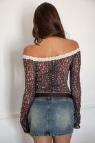Woman wearing the TIC TOC TC31579 BAMBELLE off-the-shoulder top featuring a deer-inspired mesh print, lace trim neckline, and long bell sleeves paired with a distressed denim mini skirt