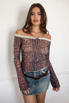 Woman wearing the TIC TOC TC31579 BAMBELLE off-the-shoulder top featuring a deer-inspired mesh print, lace trim neckline, and long bell sleeves paired with a distressed denim mini skirt