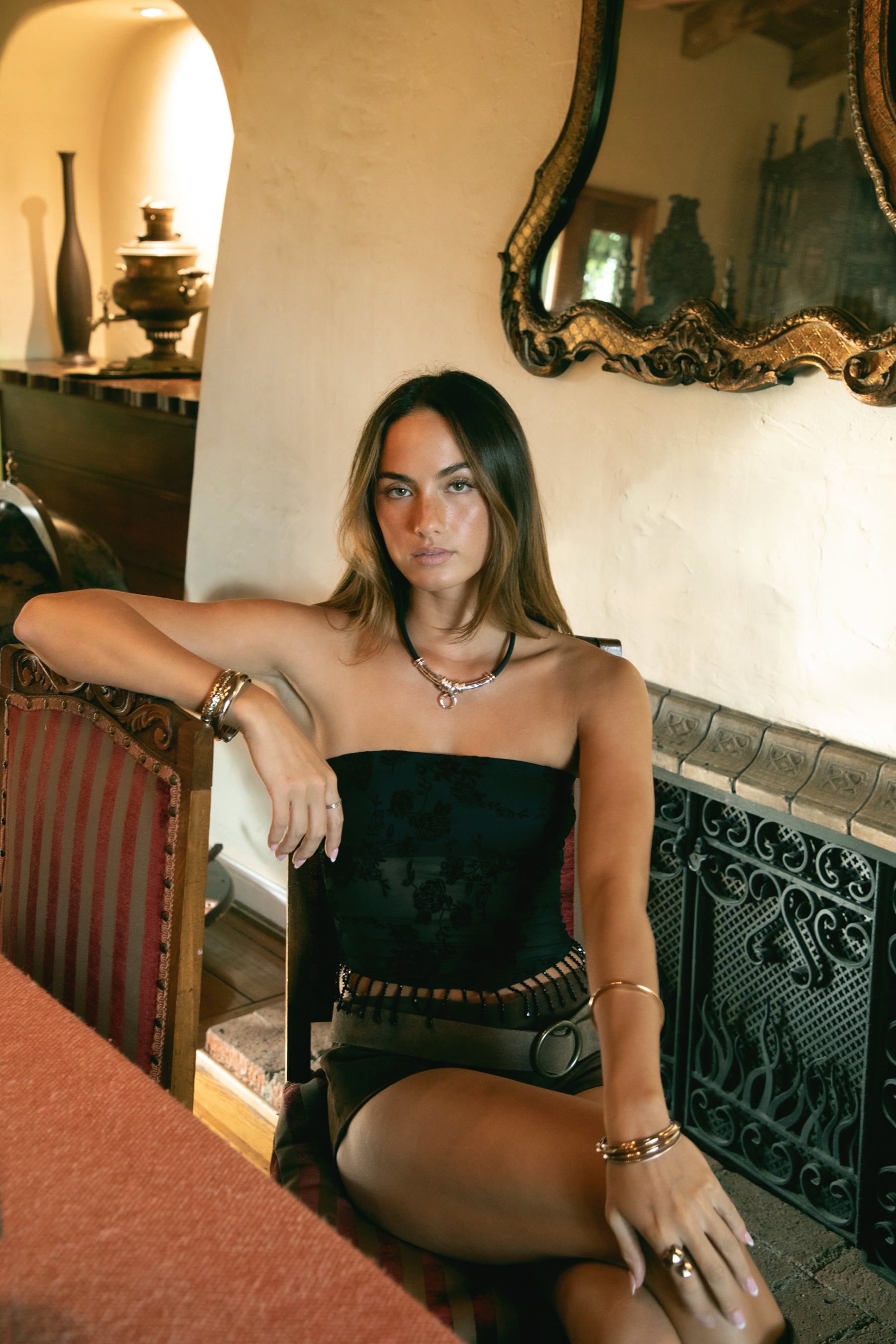 Woman wearing TIC TOC TC31585 MIRABELL flocked mesh sequin beaded bandeau top with floral detailing and side zipper closure in color black paired with suede brown shorts and boots in an indoor setting. 