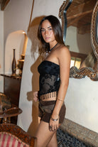 Woman wearing TIC TOC TC31585 MIRABELL flocked mesh sequin beaded bandeau top with floral detailing and side zipper closure in color black paired with suede brown shorts in an indoor setting. 