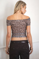 Woman wearing the TIC TOC TC31604 JAVAYA leopard mesh off-the-shoulder top featuring short cap sleeves and an asymmetrical hemline with matching brown capri pants