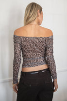 Woman wearing the TIC TOC TC31605 LEORA leopard mesh off-the-shoulder top featuring a straight neckline, asymmetrical hem, and long fitted sleeves withbrown capri pants