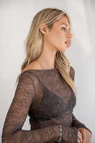 Woman wearing a TIC TOC TC31606 MIRELLE grey stretch sheer lace long sleeve top featuring a wide boat neckline, fitted sleeves, and see-through lace fabric, and brown cargo pants against a white background.