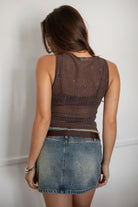 Woman wearing a brown mesh top and denim skirt against a plain background