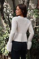 Woman wearing TIC TOC TC31678 LETTIE oatmeal sweater knit V-neck cardigan with flared sleeves, cropped peplum hem, and ribbed stretch fabric with dark denim jeans in an outdoor setting