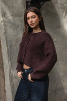 Woman wearing TIC TOC TF31833 ISOLDE brown wool-blend button down cardigan with boxy cropped fit, ribbed trim, and marled knit texture paired with dark jeans against a textured wall.