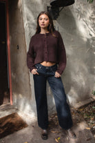 Woman wearing TIC TOC TF31833 ISOLDE brown wool-blend button down cardigan with boxy cropped fit, ribbed trim, and marled knit texture paired with dark jeans and boots against a textured wall.