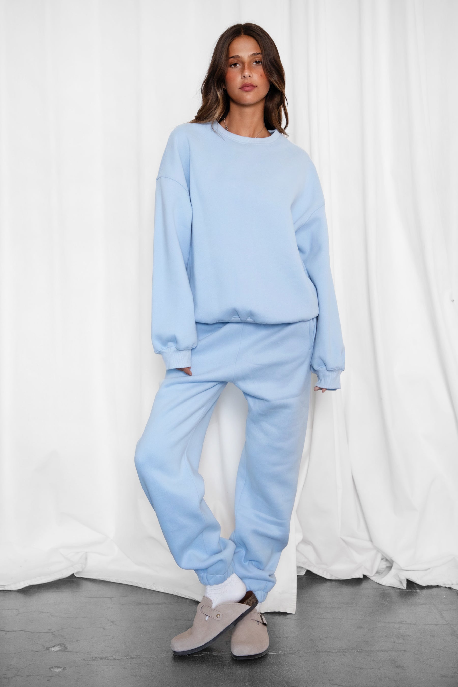 Person wearing a light blue tracksuit against a white curtain background