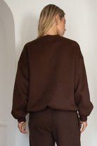 Person wearing a brown sweatshirt and pants in a minimalistic setting