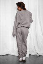 Person wearing a gray sweatshirt and pants against a white curtain background