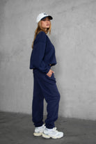 Person wearing a navy tracksuit and white sneakers against a gray background