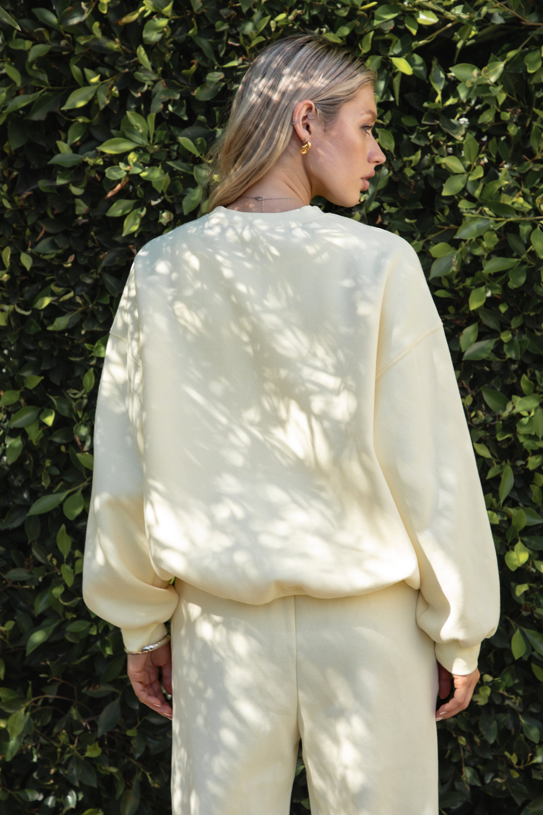 Woman wearing a yellow colored outfit standing against a green leafy background