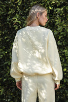 Woman wearing a yellow colored outfit standing against a green leafy background