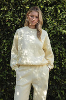 Woman wearing a yellow colored outfit standing against a green leafy background